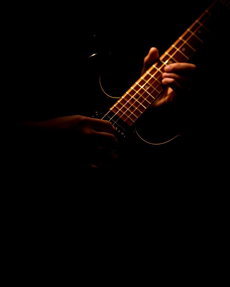 Guitarist's hands on an electric guitar lit in gold